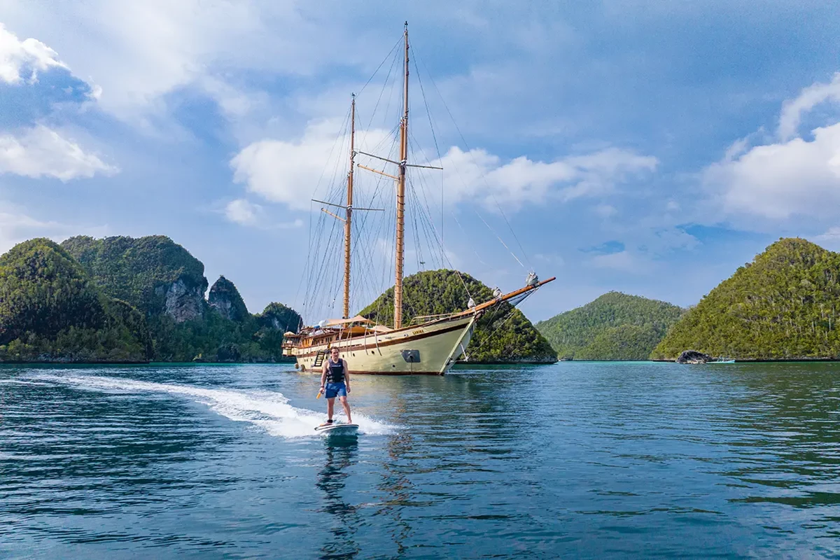 a man parasurfing in front of a old sailing ship in indonesia